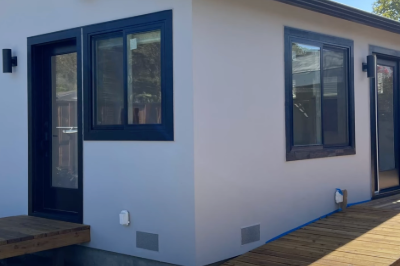 Modern detached Accessory Dwelling Unit (ADU) with a white exterior and black-framed windows, situated in a residential backyard.