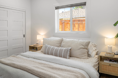 Cozy bedroom with white decor, large bed, and a potted plant by the window.