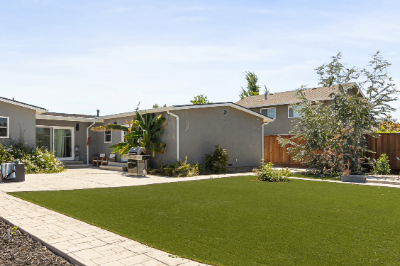Spacious backyard with artificial turf, patio area, and lush landscaping.
