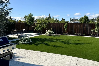 Beautifully landscaped backyard featuring a lush green lawn, stamped concrete patio, and outdoor barbecue area.