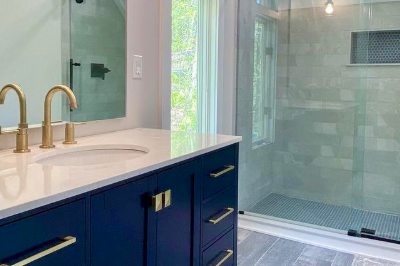 Modern bathroom remodel featuring a navy blue vanity with gold fixtures and a large walk-in shower.